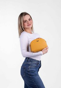 Yellow textured handbag with a rounded shape, featuring a zipper closure and brand logo, held by a model wearing a white long-sleeve top.