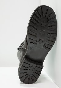 Černá kožená podrážka boty s texturovaným vzorkem obsahujícím hvězdné motivy a vyvýšeným logem. Velikost je označena jako 37 na boku.