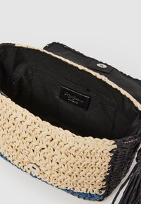 Torba pleciona w dwukolorowym wzorze: naturalnym i czarnym z niebieskimi akcentami. Wnętrze ma czarne wykończenie z tkaniny oraz małą metkę.