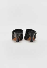 Mule-uri cu toc înalt, negre, țesute, cu un finisaj texturat și un toc curbat, lucios, negru. Design cu spatele deschis și interior neted.