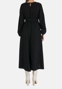 Musta midi mekko, jossa on pitkät hihat, kireä vyötärö ja avainaukko takana, yhdistettynä kiiltäviin valkoisiin paksupohjaisiin saappaisiin.