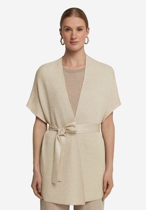 Beżowy sweter typu wrap z krótkimi rękawami, wiązany w talii, z otwartym przodem i subtelnym połyskiem. W zestawie z lekką bluzką.