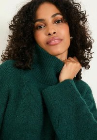 Türkis gestrickter Pullover mit hohem Kragen und gerippten Bündchen. Verfügt über strukturierte Muster und eine weiche, flauschige Textur. Nahaufnahme des Kleidungsstücks.