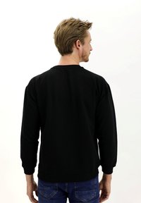 Sudadera negra de manga larga, con cuello redondo y puños de canalé. La tela parece suave, con una textura lisa y sin patrones visibles.
