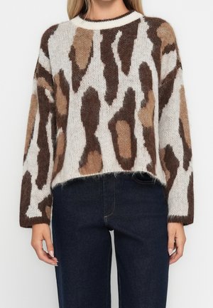 Femme portant un pull en maille duveteuse avec un imprimé animal abstrait marron et beige et un jean taille haute bleu foncé.