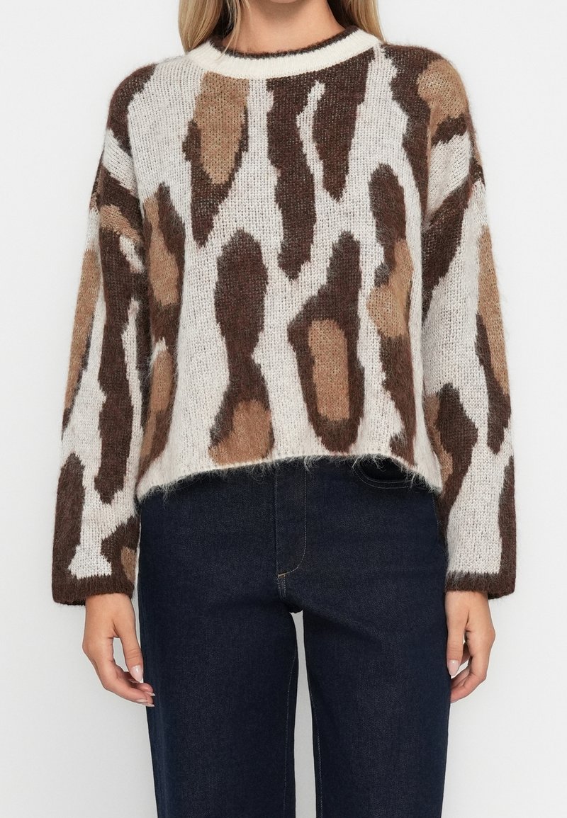 Femme portant un pull en maille duveteuse avec un imprimé animal abstrait marron et beige et un jean taille haute bleu foncé.