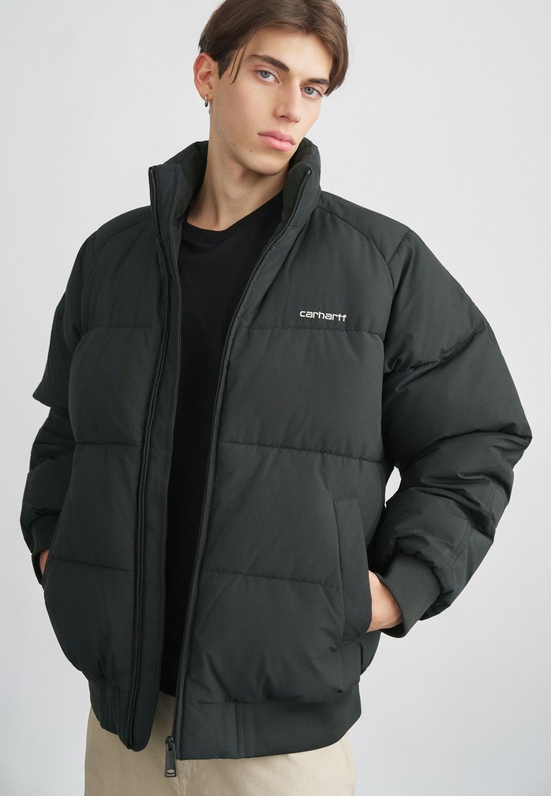 Giacca a vento nera con collo alto, texture trapuntata, chiusura con zip e logo Carhartt sul lato sinistro del petto. Polsini e orlo a costine.