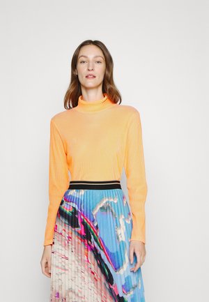 Haut orange à manches longues avec un col montant, associé à une jupe plissée arborant un motif abstrait coloré et une taille noire.