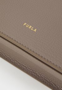 Furla kožni novčanik u taupe boji s teksturiranim završetkom; sadrži urezani logo u zlatnoj boji. Kompaktni oblik, minimalno šivanje i mekani osjećaj.