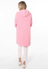 Rosa gestrickte lange Strickjacke mit Kapuze, mit einem lässigen Schnitt und weicher Textur, kombiniert mit hellen, verkürzten Hosen und Espadrilles.