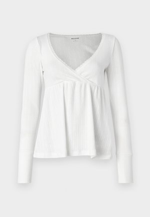 Λευκή μπλούζα με μακριά μανίκια και σχέδιο σε τύπου περιτύλιξης, πλεκτή υφή, βαθύ V-λαιμόκοψη και ροή στο τελείωμα. Διαθέτει διακοσμητική δαντέλα κατά μήκος του λαιμόκομματος.