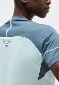 Άνδρας φοράει αθλητική μπλούζα διχρωμίας σε αποχρώσεις του μπλε με μικρό λογότυπο ζώου στο πάνω μέρος της πλάτης, εμφανιζόμενος από πίσω και σε προφίλ πλευράς.