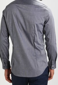 Grå mönstrad skjorta med lång ärm, rak skärning, knäppte manschetter och sidofickor. Tillverkad av vävd textil med en slät struktur.