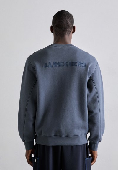 Sudadera azul oscura con corte relajado, que presenta el texto bordado "J. Lindeberg" en la parte posterior. Fabricada en un tejido suave, con puños y dobladillo acanalados.
