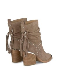 Botas de ante hasta el tobillo en beige con diseño arrugado, detalle de flecos, tachuelas metálicas y un tacón de madera apilado. Punta abierta con un frente redondeado.