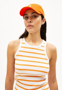 Gestreiftes Tanktop in Weiß und Orange mit gerippter Textur, kombiniert mit einer orangenen Baseballmütze, die ein weißes Logo zeigt.