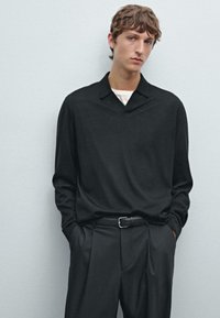 Sort langærmet skjorte med krave, kombineret med skræddersyede sorte bukser og et læderbælte, med en ensfarvet tekstur og minimalistisk design.