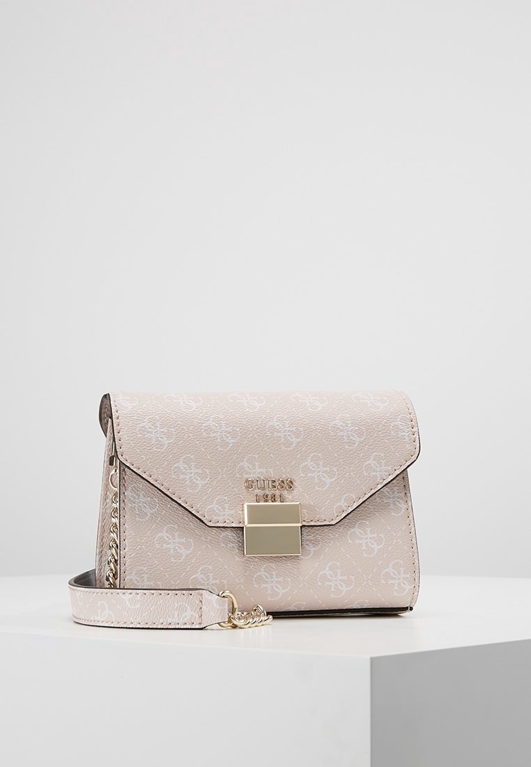 Jasnoróżowy portfel na nadgarstek Guess z powtarzającym się wzorem monogramu, złotą klamrą i dołączonym paskiem, leżący na białej powierzchni.