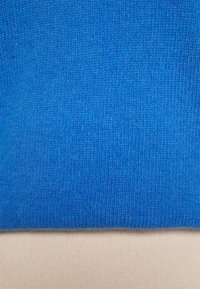 Vista ravvicinata di un tessuto a maglia blu sovrapposto a un tessuto a maglia beige, che mostra la texture e i dettagli dei punti di entrambi i materiali.