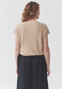 Top corto de manga corta beige con un escote redondo, combinado con una falda negra. Tejido texturizado visible en la vista trasera.