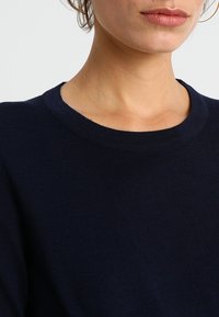 Pull en maille bleu marine avec un col rond et une texture côtelée. Vue en gros plan montrant les détails du tissu et de la confection.