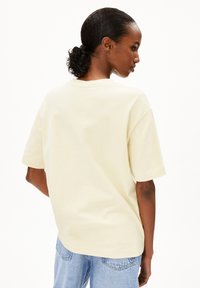 Kurzärmliges, Rundhals-T-Shirt aus weichem, hellgelbem Baumwollstoff. Hat eine lockere Passform und ein einfaches Design, kombiniert mit hellblauen Jeans.