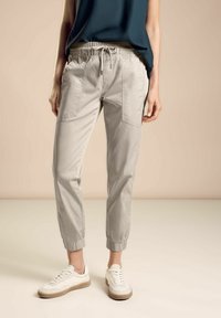 Ljust grå joggerbyxor med elastiskt midjeband och sidofickor, tillsammans med vita sneakers. Slät bomullstyg med samlade manschetter.