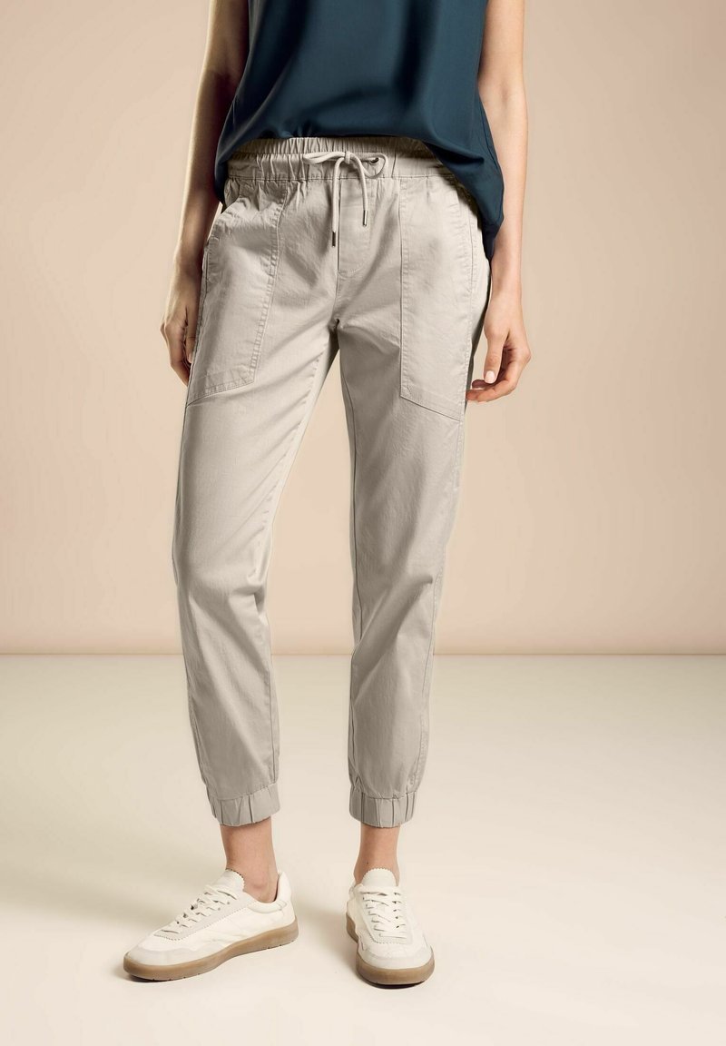 Ljust grå joggerbyxor med elastiskt midjeband och sidofickor, tillsammans med vita sneakers. Slät bomullstyg med samlade manschetter.