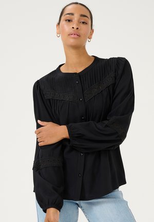 Zwarte blouse met geplooide textuur, kantaccenten en manchetten. Heeft een knoopsluiting aan de voorkant en een ronde halslijn.