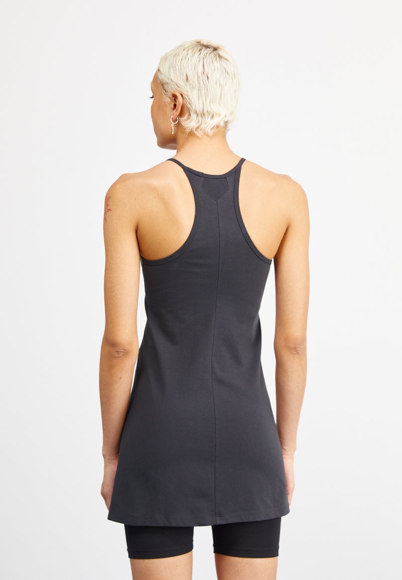 Czarna sukienka sportowa z plecami w stylu racerback, wykonana z gładkiego materiału. Posiada dopasowany gorset i rozkloszowany dół, noszona na czarnych szortach.