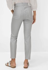 Graue Slim-Fit-Hosen mit glatter Textur, hoher Taille und zwei Gesäßtaschen, kombiniert mit hellen Sandalen.