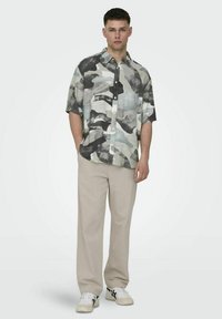 Korte mouwen overhemd met een grijs en zwart abstract patroon, gecombineerd met lichtbeige pantalons en witte sneakers. Casual pasvorm.