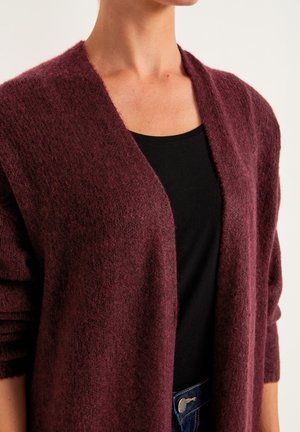 Bordeaux cardigan gemaakt van zachte, gestructureerde stof, met een open voorkant en ontspannen mouwen, gestyled over een zwarte top.