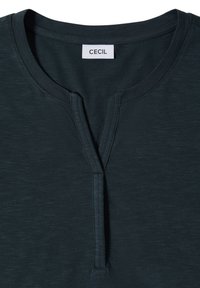 Chemise vert foncé avec encolure ronde et courte fente à l'avant, avec une étiquette blanche marquée "CECIL" à l'intérieur du col.