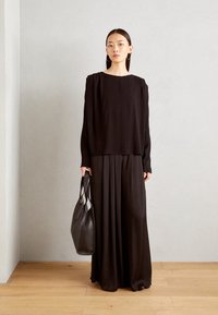 Maglietta nera a maniche lunghe con una vestibilità rilassata e spalle plissettate, abbinata a una lunga gonna nera fluida. Porta una grande borsa in pelle nera.