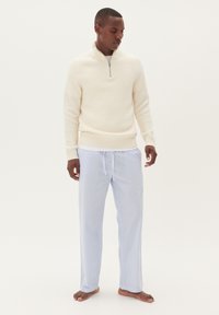 Off-white rebrasto pulover s collarem na polovično zadrgo, v kombinaciji s svetlo modrimi črtastimi pižamami. Mehka tkanina, sproščen kroj in sproščen videz.
