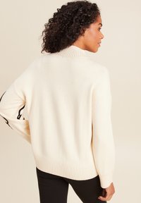 Maglione color crema con colletto e orlo a costine. Le maniche presentano dettagli neri. Tessuto morbido, vestibilità comoda e maniche lunghe.