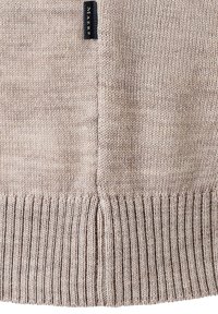 Beige pletený svetr s ribovým lemem a detaily bočního švu. Obsahuje černou označenou nášivku na boku, která předvádí strukturovanou přízi.