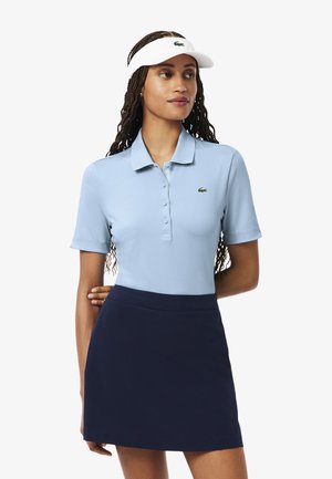 Polo shirt bleu clair à manches courtes et col, avec un logo vert. Assorti à une jupe bleu marine et une visière blanche.