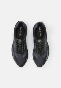 Baskets athlétiques noires avec tige en mesh texturé, accents réfléchissants et lacets noirs. Logo "Paul Smith" imprimé sur la languette.