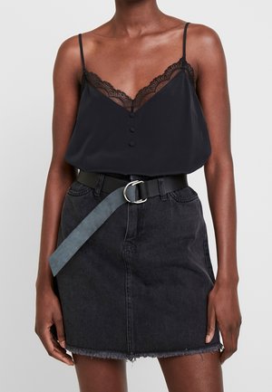 Vrouw draagt een zwart kanten topje en een zwarte spijkerbroek rok met rafelige zoom en een losse blauwe riem gesp aan de voorkant.