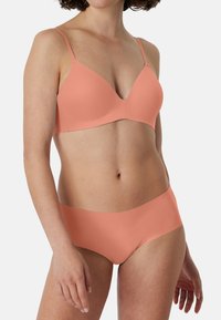 Coral-colored bra with smooth, molded cups and adjustable straps, paired with matching seamless hipster briefs made from soft fabric.