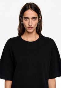 Must beebiga suurusega must T-särk ribakudumist, millel on ümar kaelus ja lühikesed varrukad. Tekstuur on sile ning ülikond on mugav.