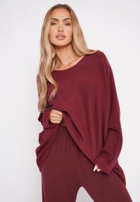Bordowy sweter dzianinowy z szerokim dekoltem i długimi rękawami, w zestawie z pasującymi spodniami. Materiał wydaje się miękki, z luźnym krojem.