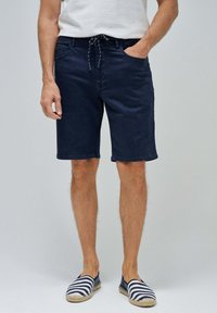 Pantalones cortos de algodón azul marino con cintura ajustable, bolsillos laterales y un corte relajado, combinados con espadrilles a rayas. Textura suave.