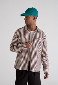 Stribet button-up skjorte i brun og cremet, lavet af tekstureret stof. Båret over en hvid t-shirt, med en brystlomme og matchende accessories.