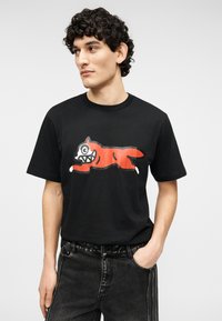 Μαύρο βαμβακερό μπλουζάκι με μεγάλο κόκκινο γραφικό ενός σκύλου που περιφέρεται με λευκές λεπτομέρειες, κοντά μανίκια, στρογγυλή λαιμόκοψη και άνετη εφαρμογή.