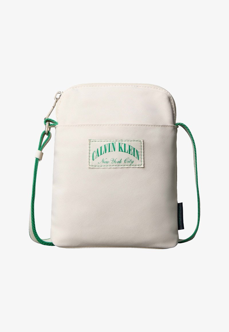 Μικρή μπεζ τσάντα χιαστί με πράσινο ρυθμιζόμενο κορδόνι, μία μπροστινή τσέπη με φερμουάρ και ένα ένθετο με το λογότυπο Calvin Klein New York City.