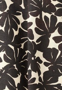 Motif floral abstrait noir sur tissu beige avec texture visible et pli subtil au milieu.