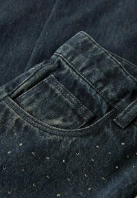 Mörka denimjeans med en framficka, sliten textur och dekorativa nitar som är arrangerade i ett prickigt mönster längs tyget.